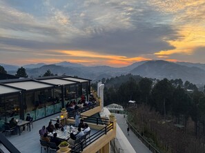 Un área de comedor al aire libre con mesas y sillas, con vistas a un paisaje montañoso.