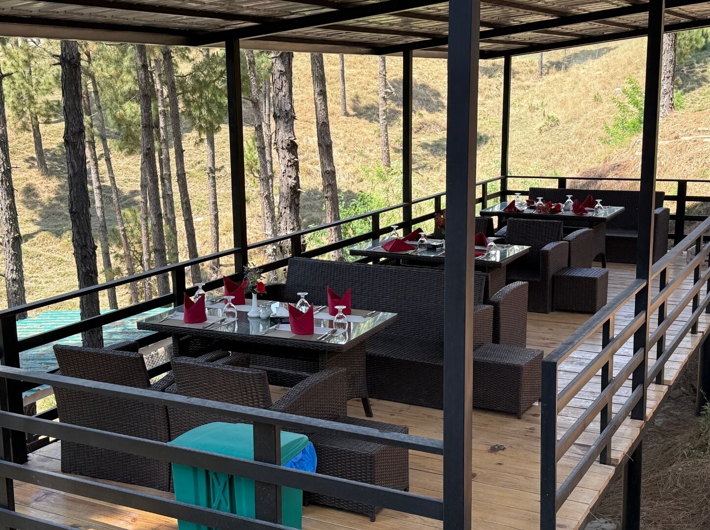 Un espace extérieur aménagé pour les repas, avec des meubles et des tables en osier, offrant une vue sur un paysage naturel composé d’arbres et de collines.
