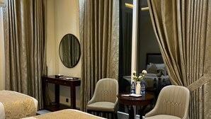 A hotel room with two beds, a desk, two chairs, a round table, and a large mirror.
