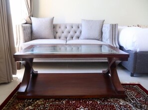 A living room with a tufted sofa, a glass-top coffee table, and a patterned rug.