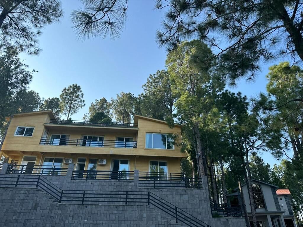 Un edificio de dos pisos con balcón, rodeado de árboles.