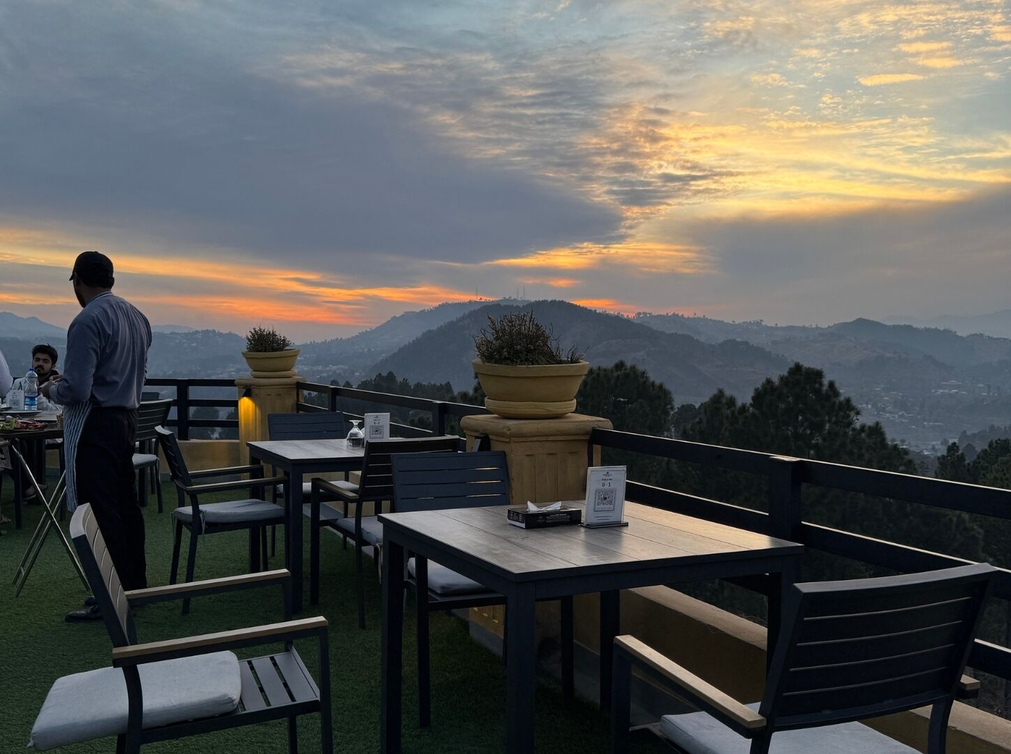 An outdoor seating area with tables and chairs, overlooking a mountainous landscape.