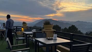 An outdoor seating area with tables and chairs, overlooking a mountainous landscape.