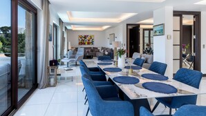 Un espace repas moderne avec une longue table, des chaises bleues et une vue sur l’extérieur.