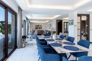 A modern dining area with a long table, blue chairs, and a view of the outdoors. - Exclusive Riviera Villa for 16 Guests | Pool & Ocean View (Saint-Jean-Cap-Ferrat)