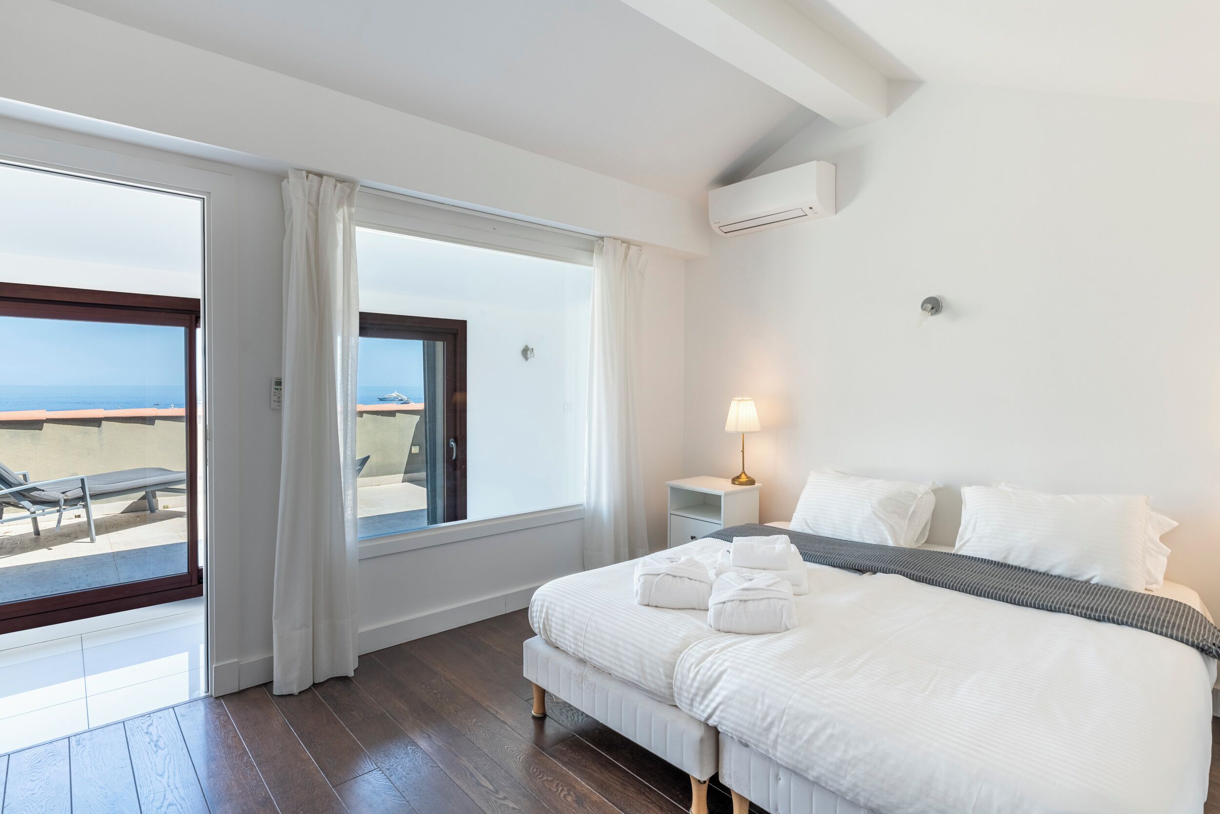 Une chambre d’hôtel avec un lit, une table de chevet avec une lampe, une fenêtre avec des rideaux et une vue sur la mer.