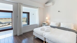 Une chambre d’hôtel avec un lit, une table de chevet avec une lampe, une fenêtre avec des rideaux et une vue sur la mer.