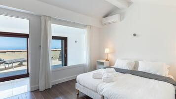 Een hotelkamer met een bed, nachtkastje met een lamp, een raam met gordijnen en uitzicht op zee.