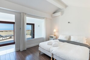 A hotel room with a bed, a bedside table with a lamp, a window with curtains, and a view of the sea. - Exclusive Riviera Villa for 16 Guests | Pool & Ocean View (Saint-Jean-Cap-Ferrat)
