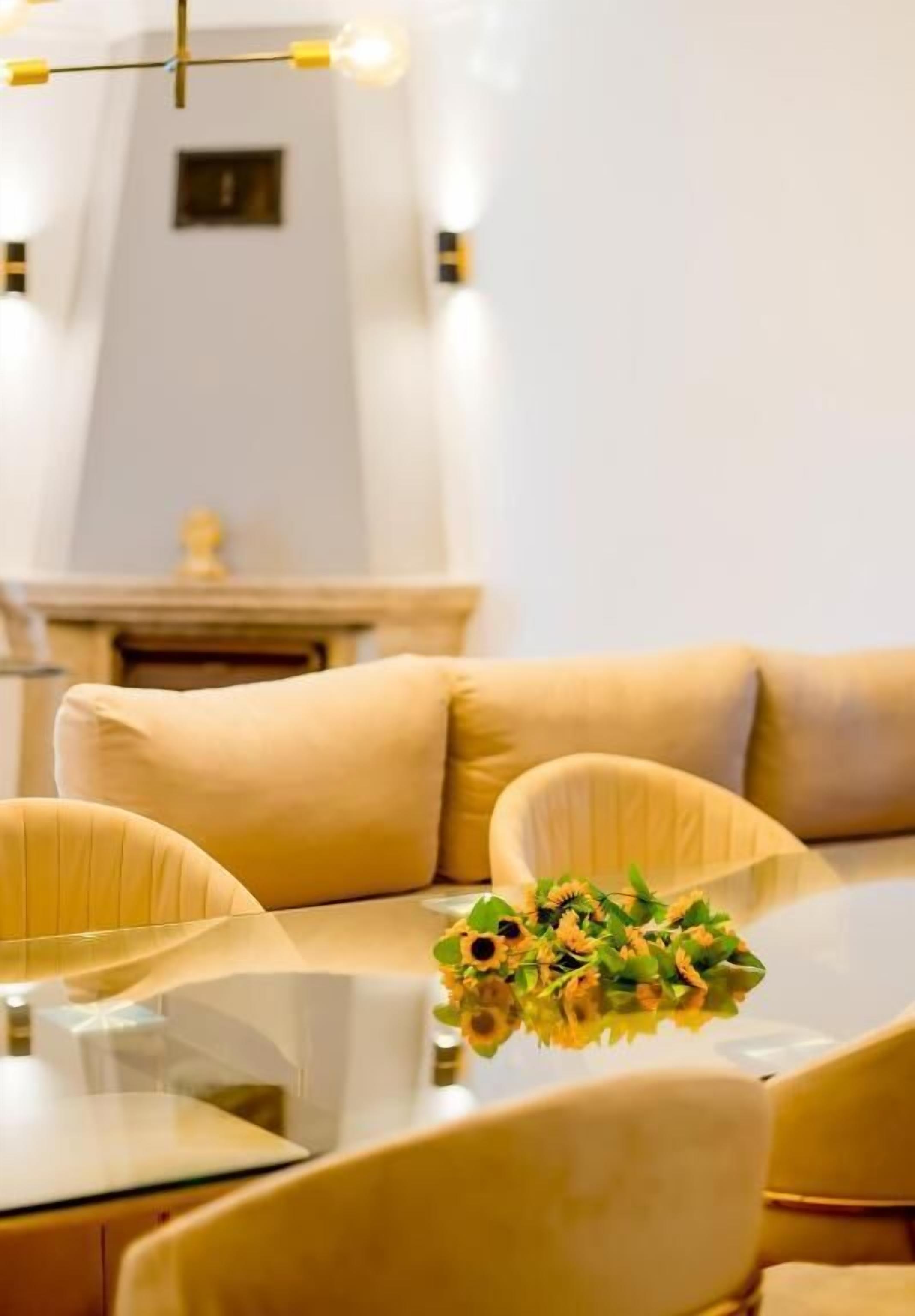A modern dining area with a glass table, beige upholstered chairs, and a vase of flowers.