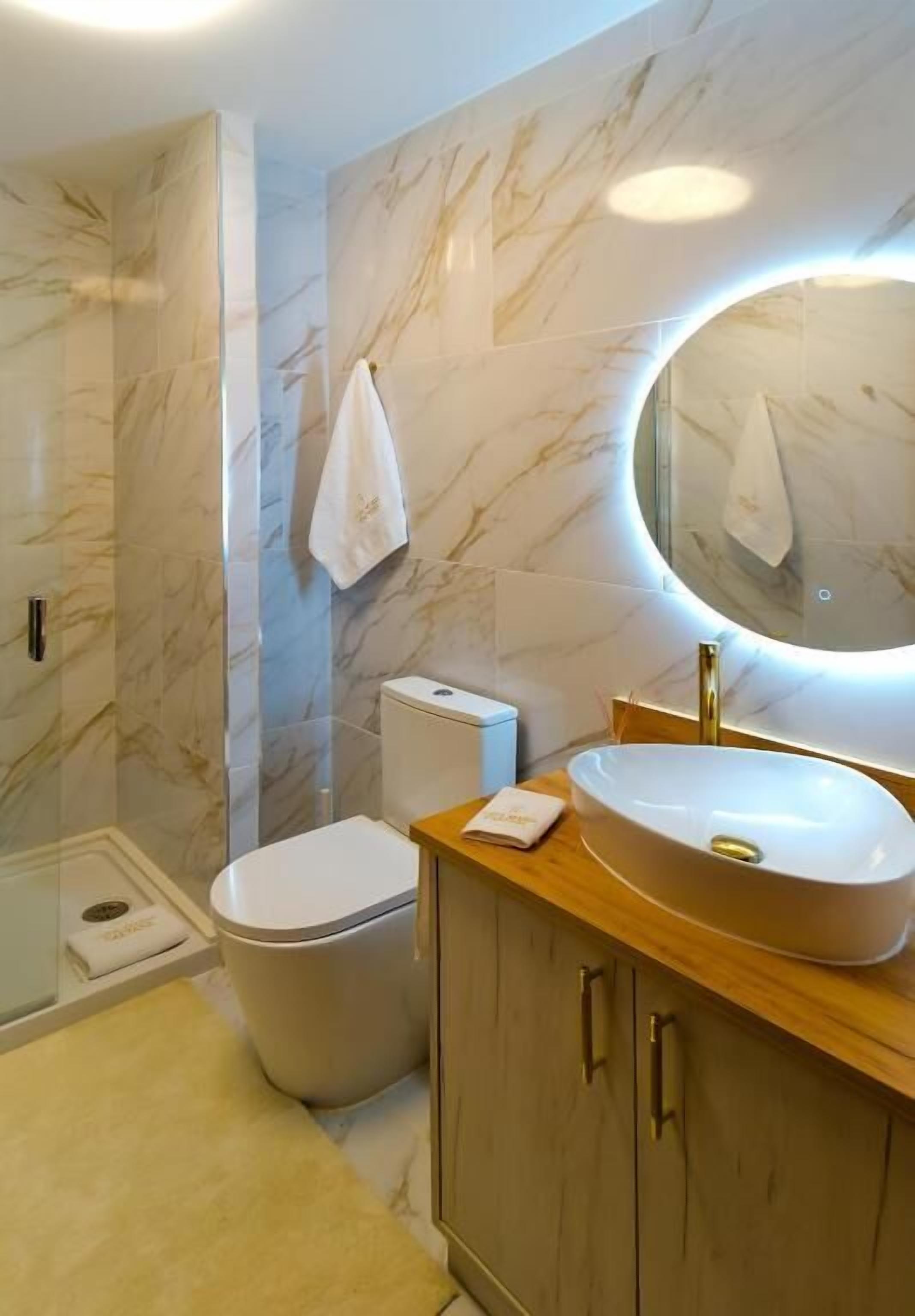 A bathroom with a marble wall, a toilet, a sink with a mirror, and a towel hanging on the wall.
