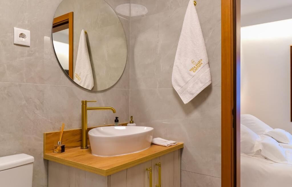 A bathroom with a round mirror, a gold faucet, a white sink, and a towel hanging on the wall.