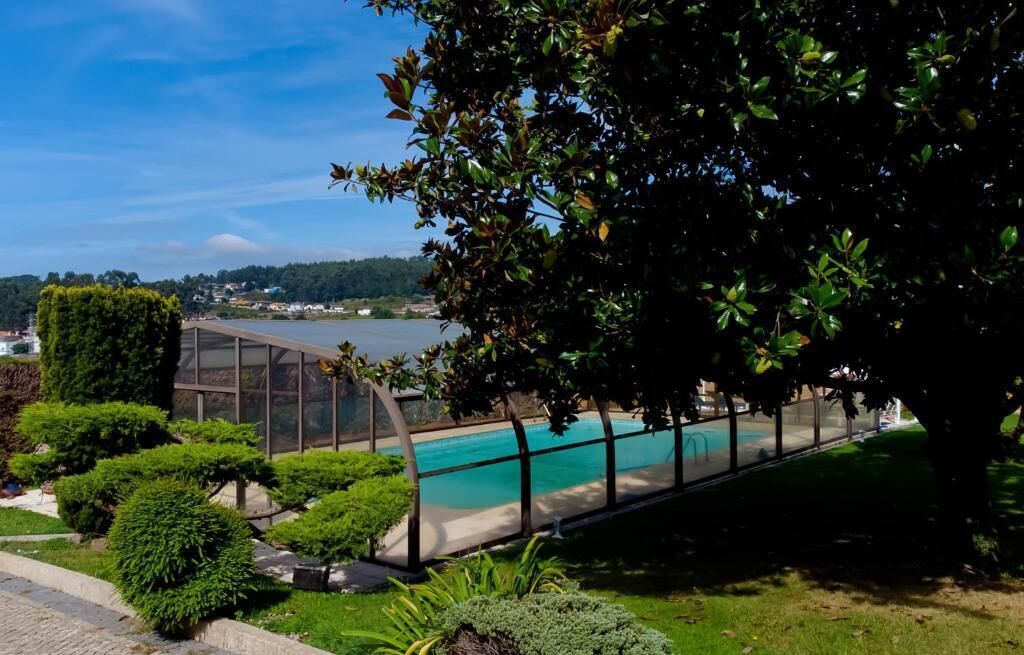 A swimming pool with a view of a body of water, surrounded by well-maintained greenery and a clear sky.