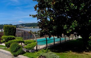 A swimming pool with a view of a body of water, surrounded by well-maintained greenery and a clear sky. - villa maria caetana (Frazão)