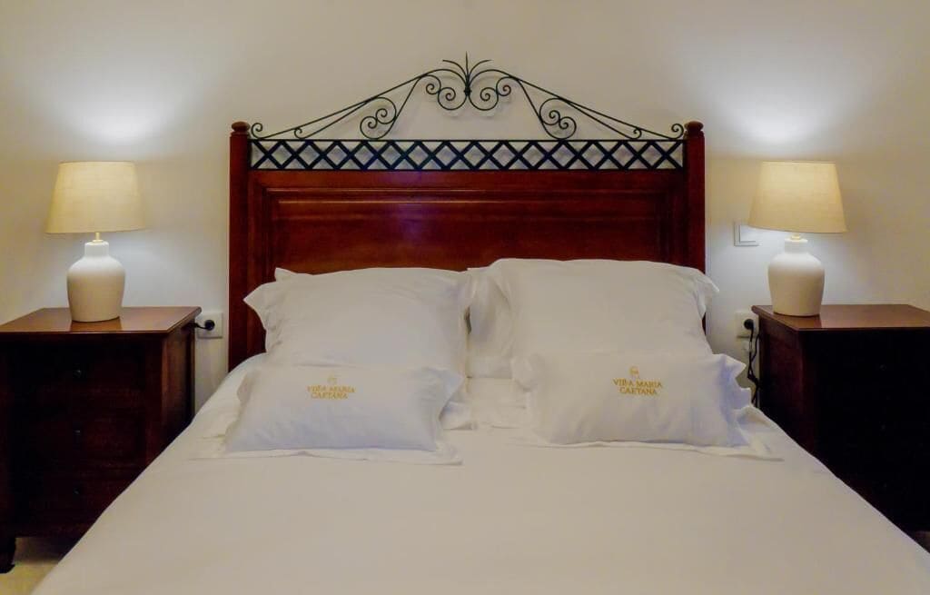 A neatly made bed with white linens and pillows, two bedside tables with lamps, and a decorative wrought iron headboard.