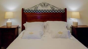 A neatly made bed with white linens and pillows, two bedside tables with lamps, and a decorative wrought iron headboard.