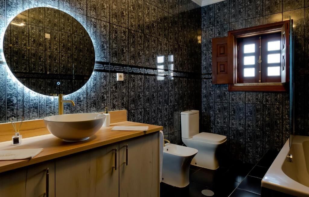 Un baño moderno con un espejo redondo, un lavabo grande tipo cuenco, un inodoro y una bañera.