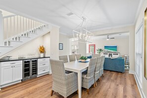 Un vaste espace de vie comprenant une table à manger, des chaises en osier, un lustre moderne et un escalier.