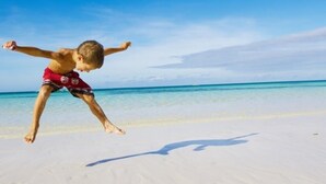 A beach scene with a child jumping on the sand. - Adorable Old Seagrove Beach Cottage Bordering Seaside Near Beach Access (Santa Rosa Beach)