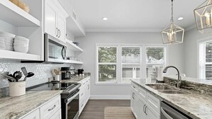 A modern kitchen with white cabinetry, a granite countertop, a built-in oven, and a dishwasher. - Adorable Old Seagrove Beach Cottage Bordering Seaside Near Beach Access (Santa Rosa Beach)