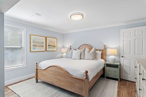 Une chambre à coucher avec un lit en bois, une table de chevet, une lampe, une porte et deux tableaux encadrés accrochés au mur.
