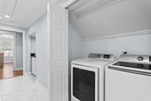 A laundry room with two white front-loading washers and dryers, a wooden floor, and a door leading to a hallway. - Adorable Old Seagrove Beach Cottage Bordering Seaside Near Beach Access (Santa Rosa Beach)