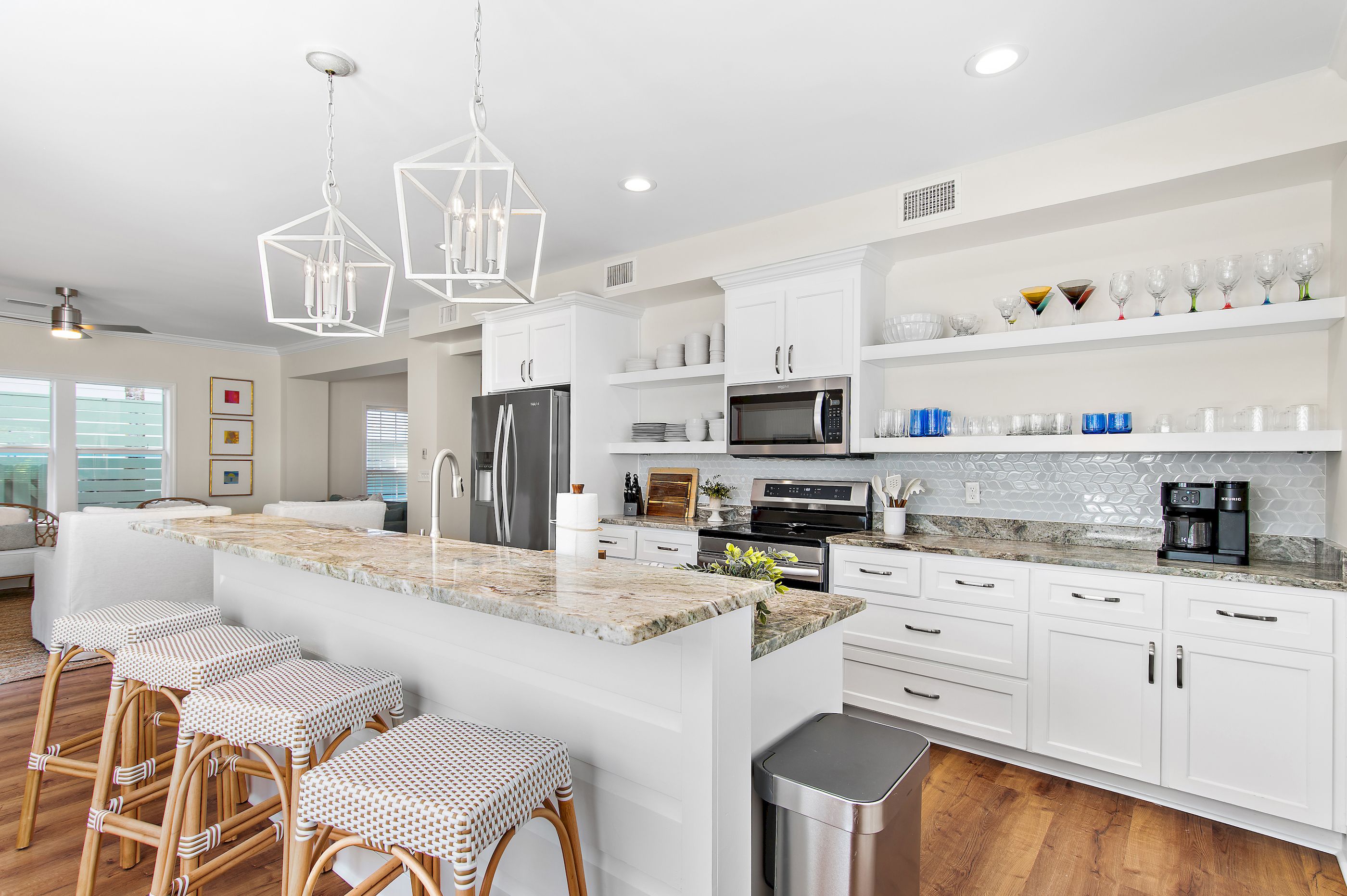 A modern kitchen with white cabinetry, a central island with bar stools, stainless steel appliances, and a coffee machine.