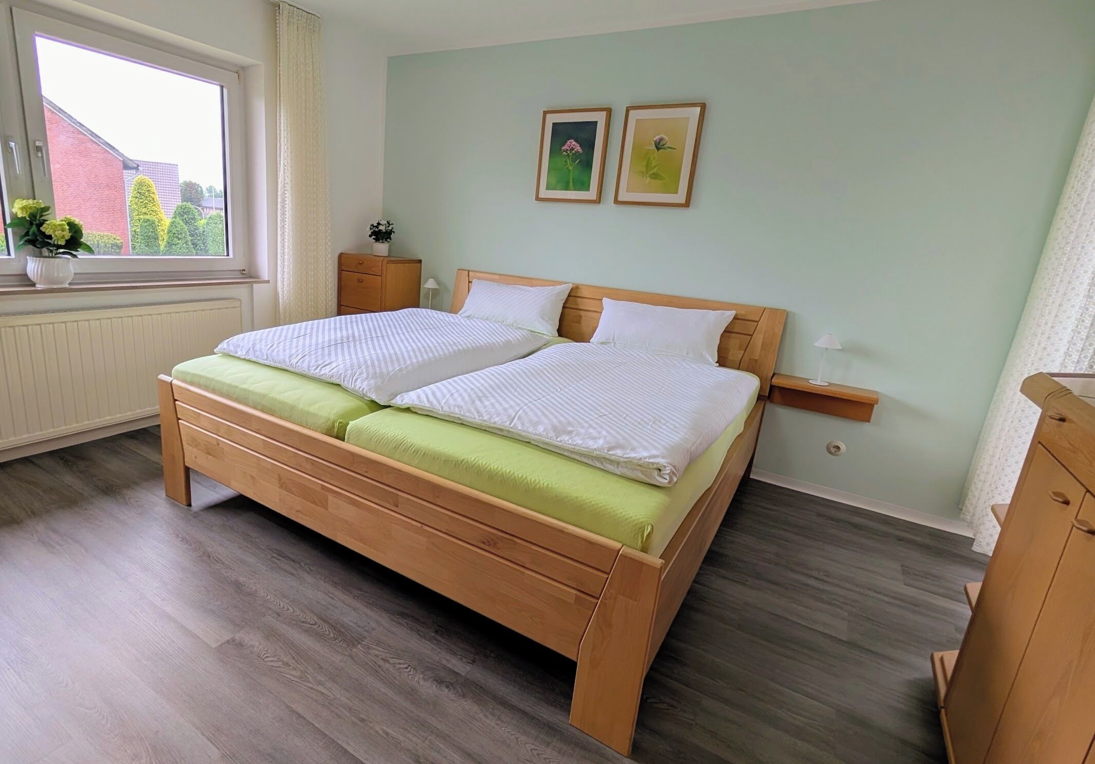 A double bed with a wooden frame and green bedding, a bedside table with a lamp, and two framed pictures on the wall.
