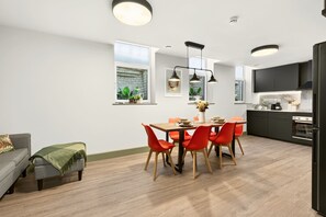 A modern kitchen with black cabinets, a built-in oven, and a dining area with a wooden table and red chairs. - Guestready - The Bridge - Wealdstone (Harrow)
