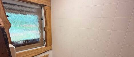 Un baño pequeño y funcional con un inodoro blanco, un marco de ventana de madera y una pared revestida de blanco.