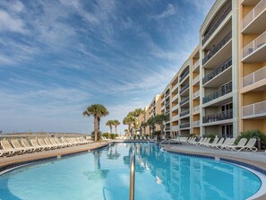 A swimming pool with lounge chairs and palm trees, surrounded by a multi-story building with balconies. - Azure #208 | Near Beach, Beautiful Views + Amenities (Fort Walton Beach)