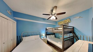 Ein Zimmer mit Etagenbett, einem Einzelbett, einem Deckenventilator und einer Wand mit Wandgemälde.