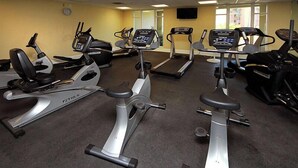 Ein Fitnessraum mit mehreren Cardiogeräten, darunter Laufbänder und Crosstrainer, mit Teppichböden und einer Uhr an der Wand.