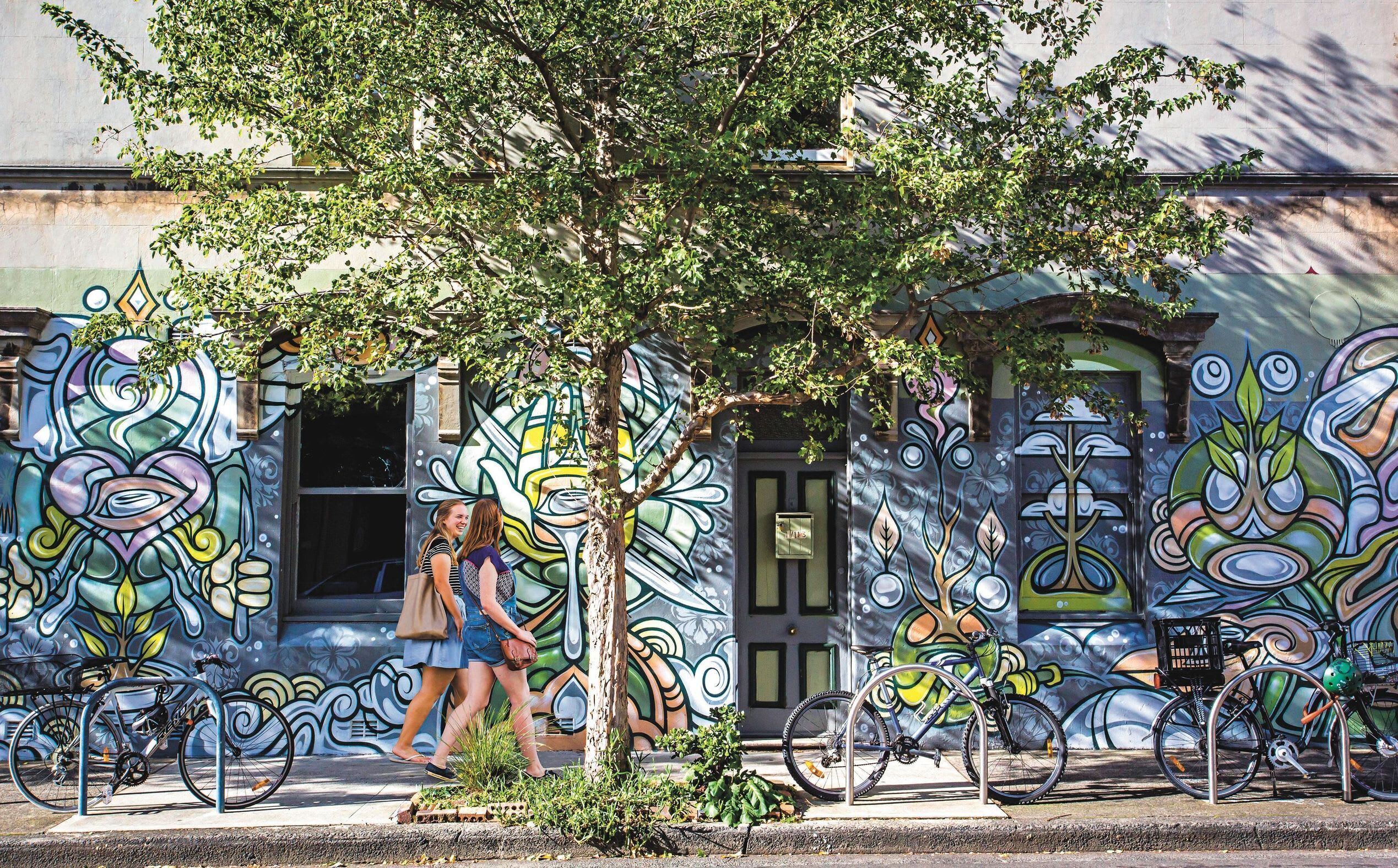 A street scene with a building featuring colorful graffiti art, a tree, and bicycles parked in front.