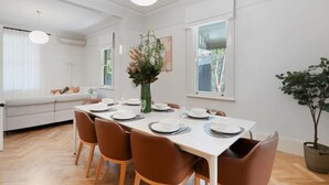 Uma área de jantar com uma mesa posta para quatro pessoas, um sofá ao fundo e um vaso de planta.
