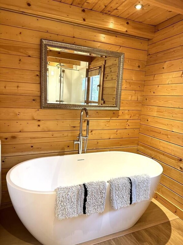 Un baño con paneles de madera, una bañera independiente, un espejo y un perchero para toallas.
