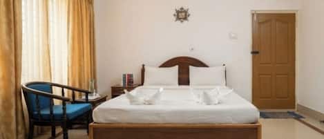 A hotel room with a wooden bed, a chair, a nightstand, and a door.