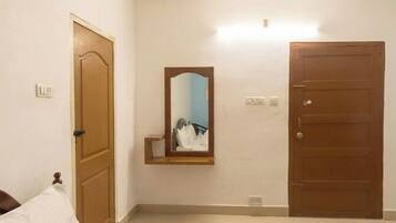 Una habitación con una cama, una puerta de madera, un espejo y una lámpara.