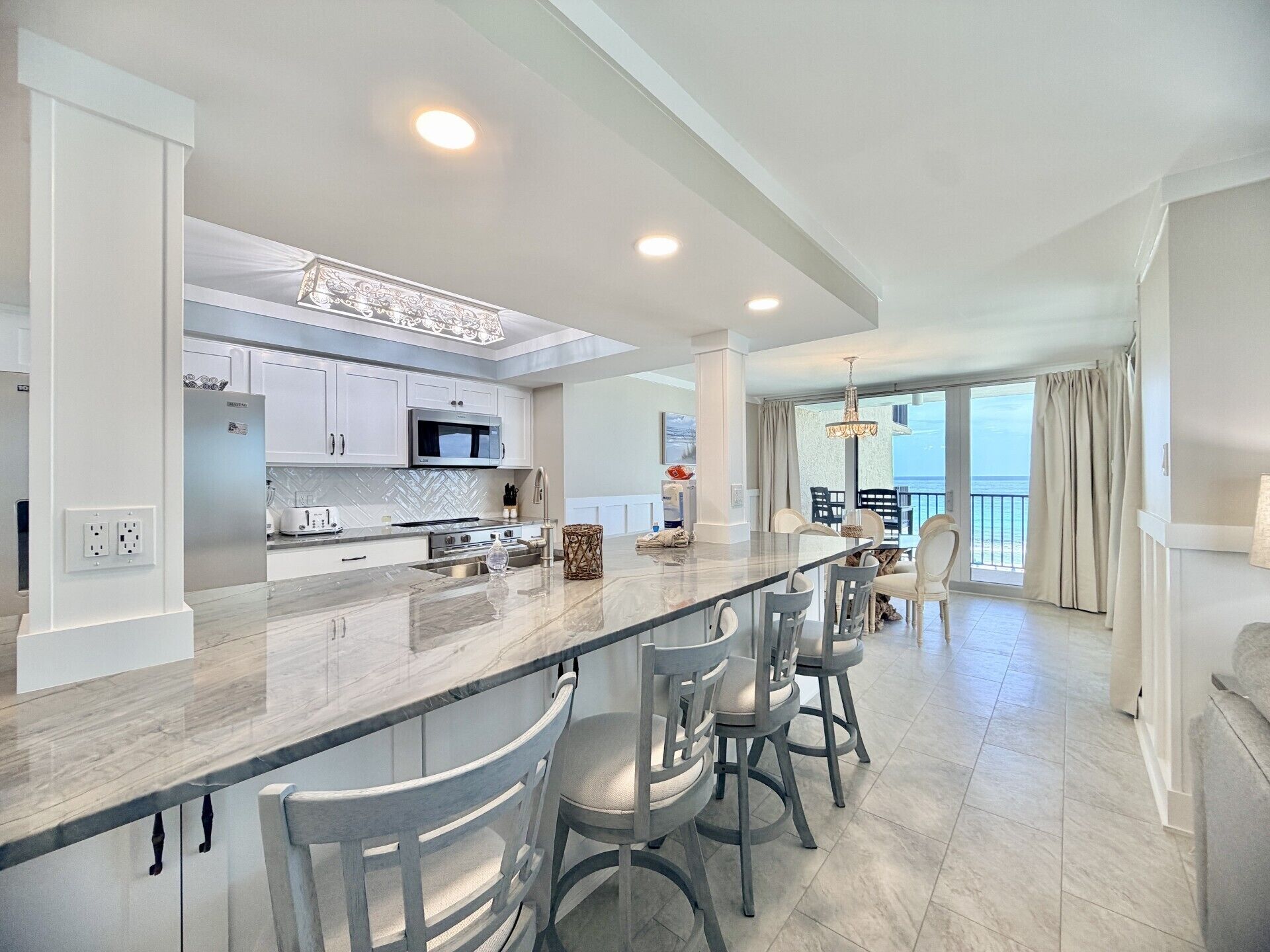 A modern kitchen with a central island, bar stools, and a view to a balcony.