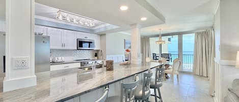 A modern kitchen with a central island, bar stools, and a view to a balcony.