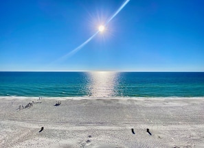 A beach with a clear sky, sun reflecting on the water, and people on the sand. - Pelican Walk 612 Beachfront BLISS! 3Bedroom Condo (Panama City Beach)