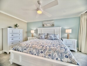 Ein Schlafzimmer mit einem Bett, Nachttischen, einem Schminktisch und einem Deckenventilator, sowie einer Wandlampe.