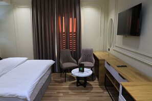 Una camera d'albergo con un letto, due poltrone, un tavolino rotondo, una scrivania e un televisore a parete.