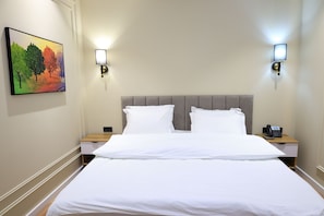 Una camera d'albergo con un letto grande, due comodini, un quadro appeso al muro e due luci a parete.