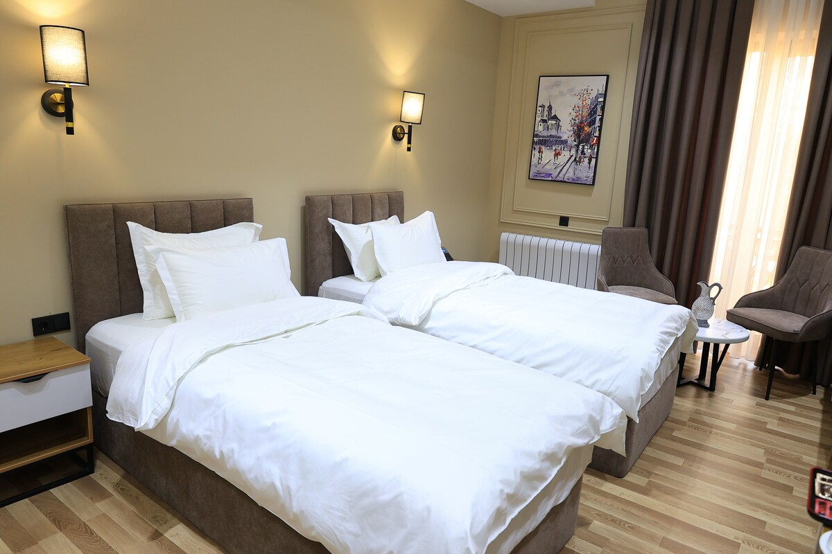 Una camera d'albergo con due letti, un comodino, una sedia e un quadro appeso al muro.