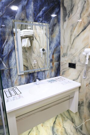 Un bagno con un mobile vanitario in marmo, uno specchio, un portascopino e un asciugacapelli.