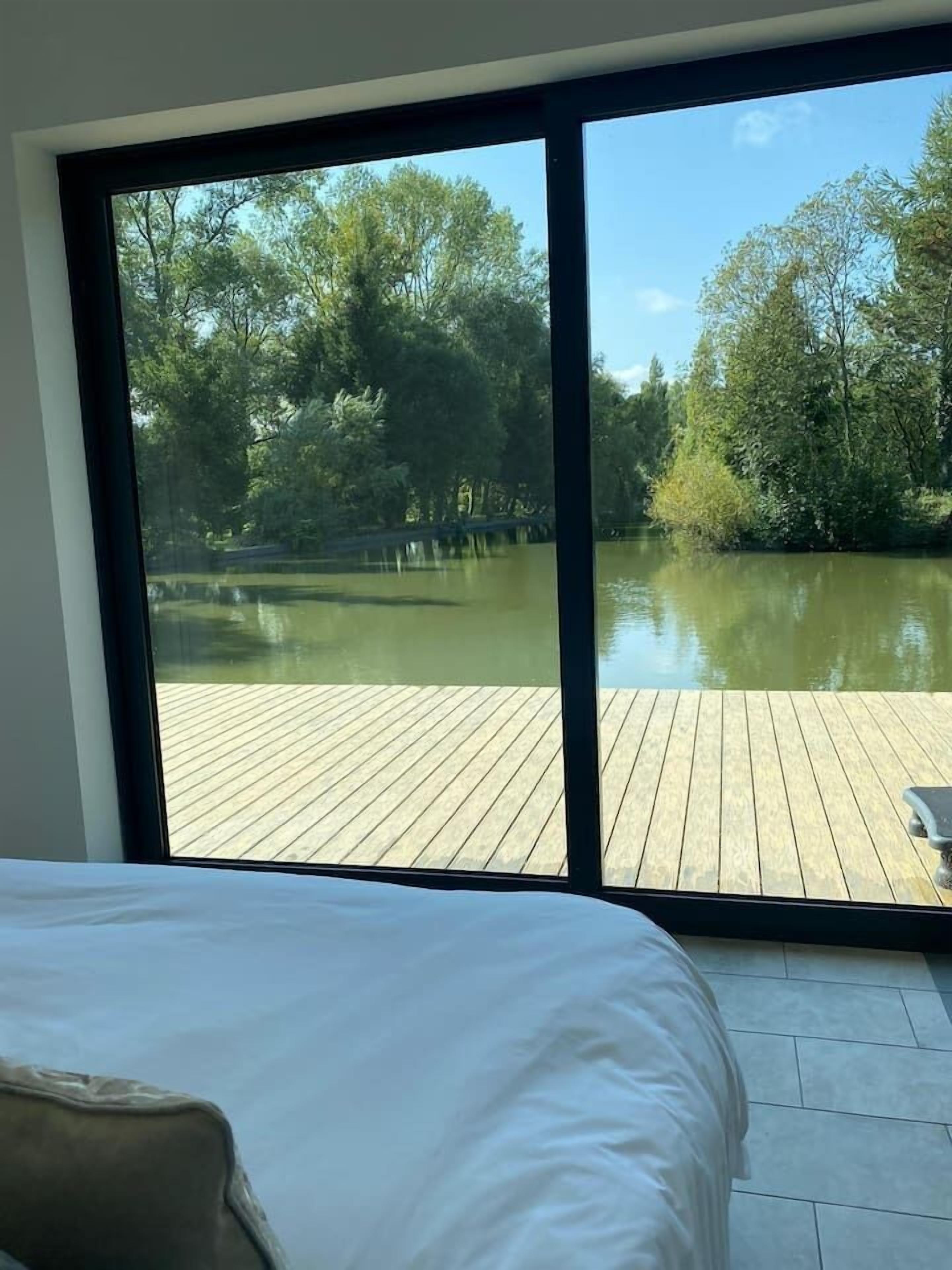 A bedroom with a large window overlooking a wooden deck and a body of water.