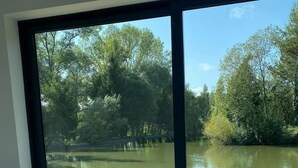 Ein Schlafzimmer mit großem Fenster mit Blick auf eine Holzterrasse und ein Gewässer.