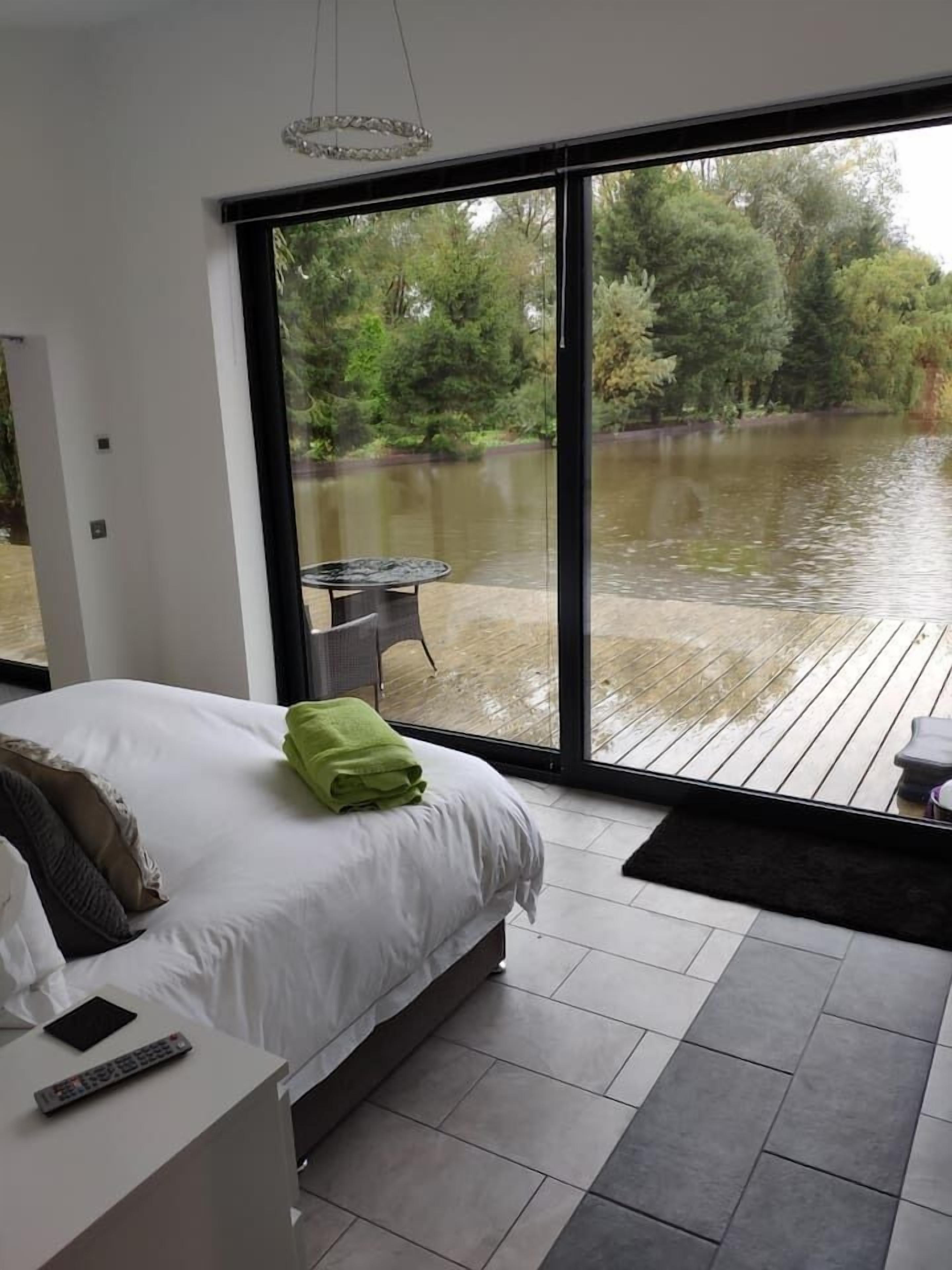 A bedroom with a large window overlooking a water body and greenery.