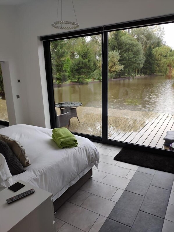 A bedroom with a large window overlooking a water body and greenery.
